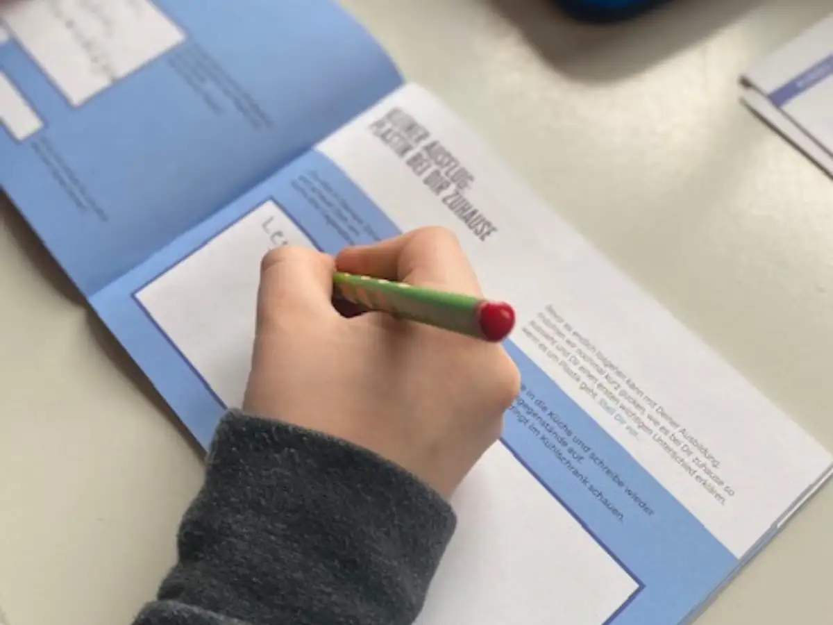 Eine Kinderhand schreibt mit einem Stift in ein Arbeitsheft.