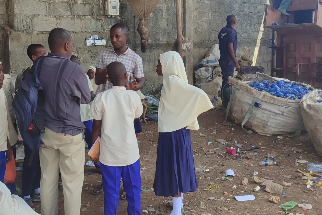 Schulkinder in Uniform besuchen auf Sansibar eine Recyclingstation mit gesammelten Plastikflaschen.