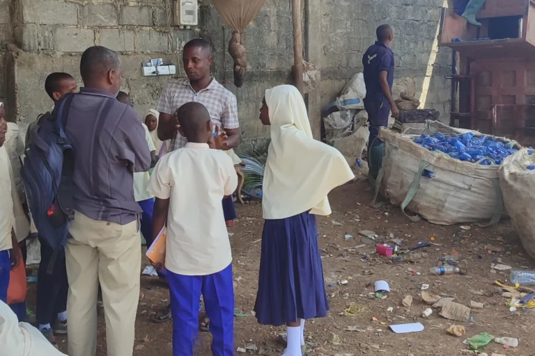 Schulkinder in Uniform besuchen auf Sansibar eine Recyclingstation mit gesammelten Plastikflaschen.