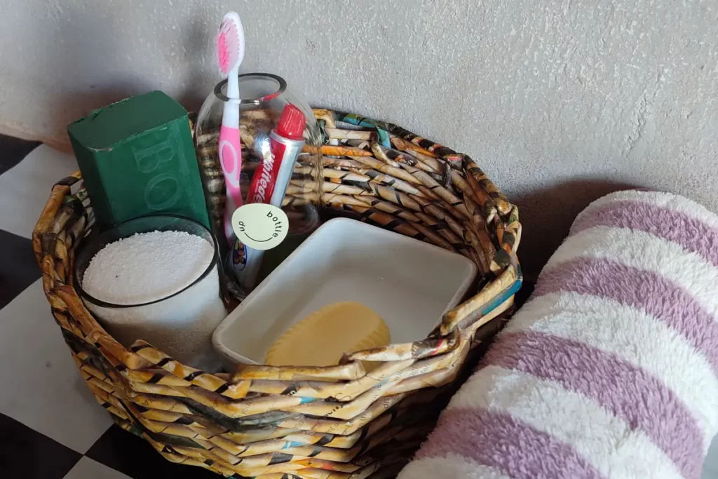 Ein geflochtener Korb mit Hygieneartikeln wie Zahnbürste, Zahnpasta und Seife, daneben ein Handtuch.