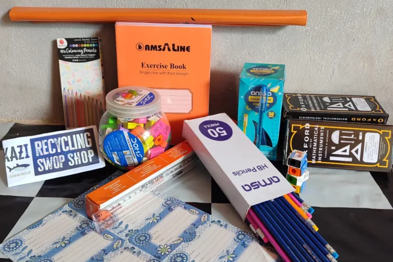 Ein Set aus Schulmaterialien wie Heften, Stiften und Lineal, daneben ein Schild „Recycling SwopShop“.