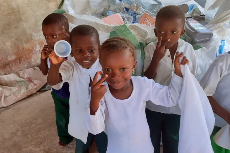 Lachende Schulkinder in Uniform vor Säcken mit gesammeltem Plastik.