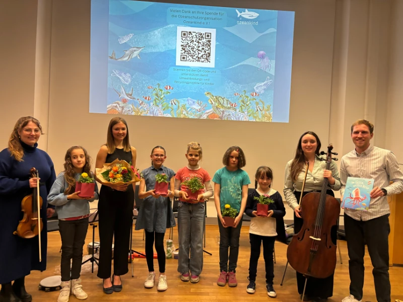 Kinder und Erwachsene mit Instrumenten und Blumen auf einer Bühne bei einem Benefizkonzert für Ozeankind.