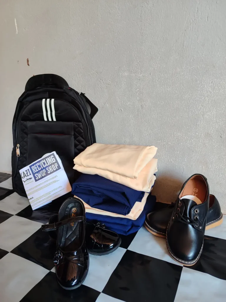 Ein Schulausstattungs-Set aus Rucksack, Uniform und Schuhen, daneben ein Schild „Recycling SwopShop“.